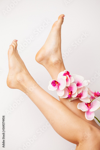 Long legs of a woman with a fresh manicure and orchid flowers