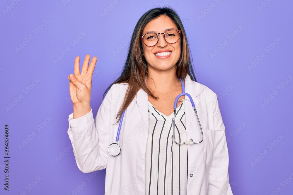 Professional doctor woman wearing stethoscope and medical coat over purple background showing and pointing up with fingers number three while smiling confident and happy.