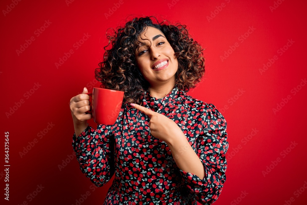 Young beautiful curly arab woman drinking mug of coffee over isolated red background very happy pointing with hand and finger Young beautiful curly arab woman drinking mug of coffee over isolated red background very happy pointing with hand and finger