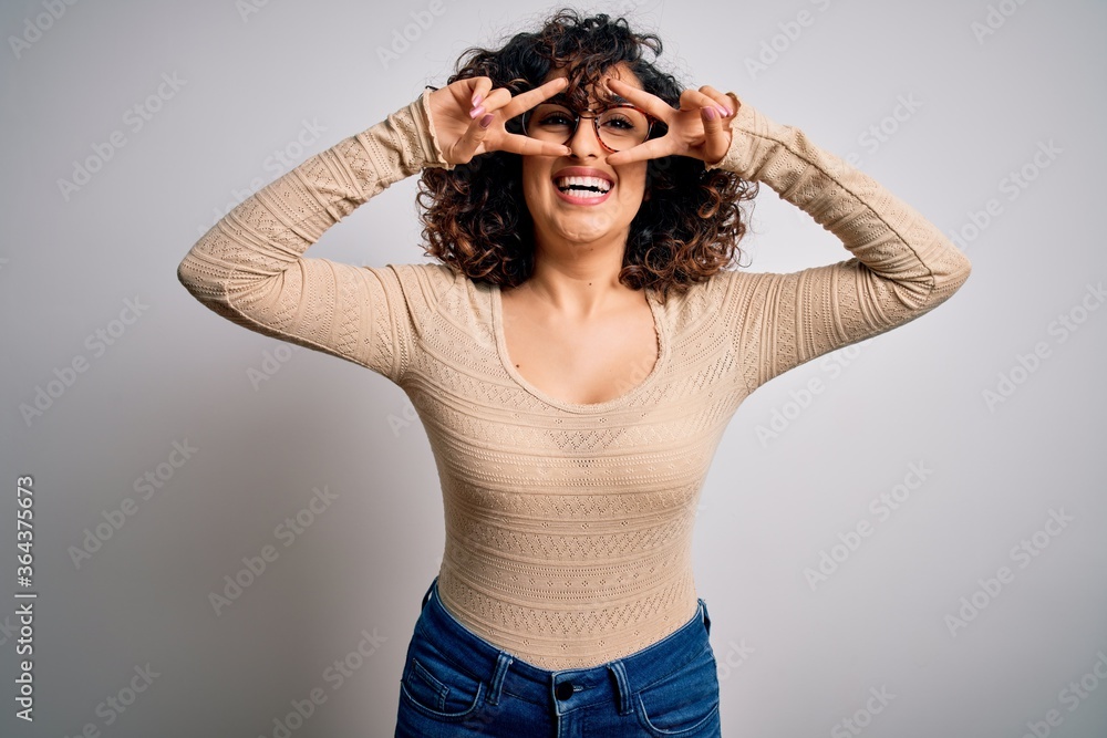 © Krakenimages.com - Young beautiful curly arab woman wearing casual t-shirt and glasses over white background Doing peace symbol with fingers over face, smiling cheerful showing victory © Krakenimages.com - Young beautiful curly arab woman wearing casual t-shirt and glasses over white background Doing peace symbol with fingers over face, smiling cheerful showing victory