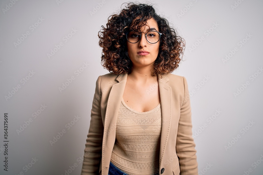 Young curly arab business woman wearing elegant jacket and glasses over white background with serious expression on face. Simple and natural looking at the camera. Young curly arab business woman wearing elegant jacket and glasses over white background with serious expression on face. Simple and natural looking at the camera.