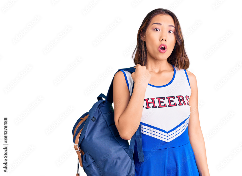 Young beautiful chinese girl wearing cheerleader uniform holding student backpack scared and amazed with open mouth for surprise, disbelief face Young beautiful chinese girl wearing cheerleader uniform holding student backpack scared and amazed with open mouth for surprise, disbelief face