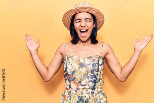 Young beautiful latin woman wearing summer hat celebrating mad and crazy for success with arms raised and closed eyes screaming excited. winner concept