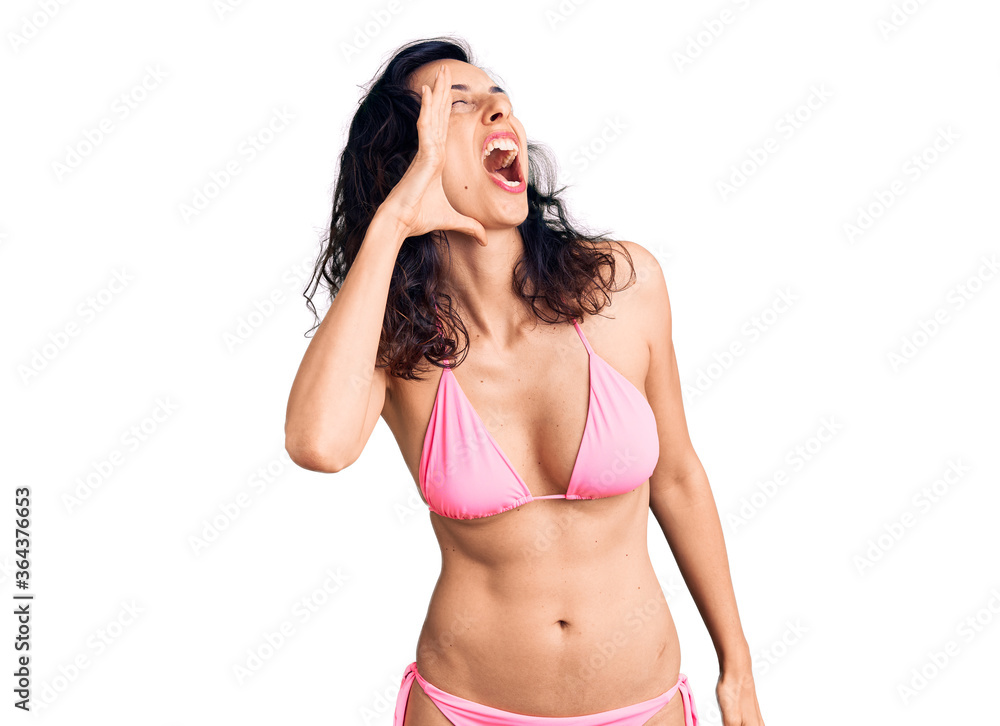 Naklejka premium Young beautiful hispanic woman wearing bikini shouting and screaming loud to side with hand on mouth. communication concept.