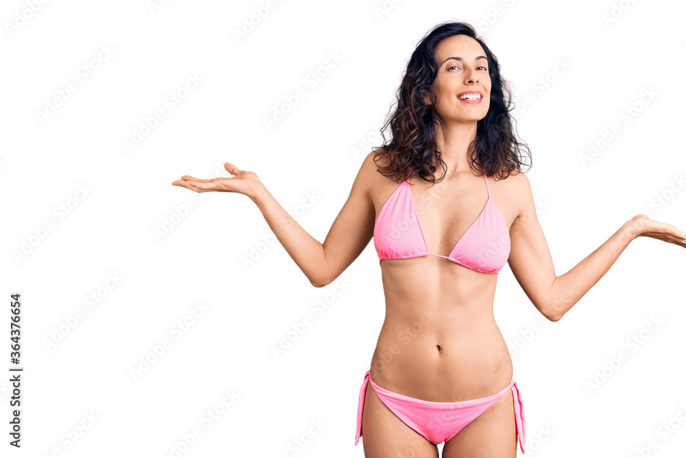 Young beautiful hispanic woman wearing bikini smiling showing both hands open palms, presenting and advertising comparison and balance Young beautiful hispanic woman wearing bikini smiling showing both hands open palms, presenting and advertising comparison and balance
