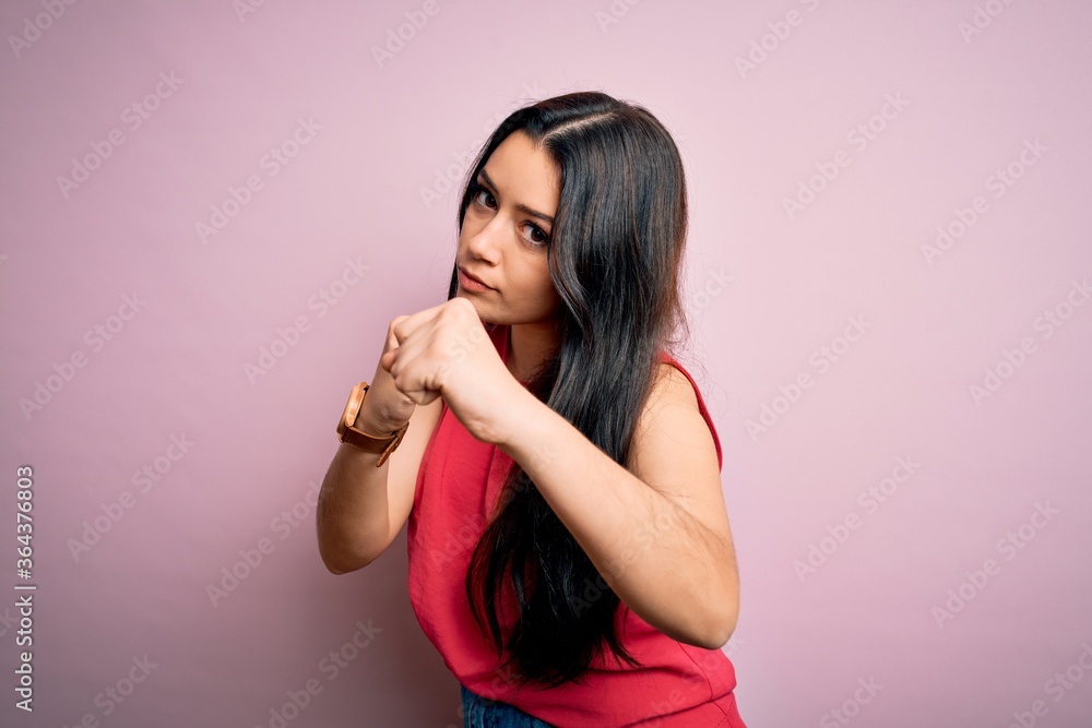 Fototapeta premium Young brunette woman wearing casual summer shirt over pink isolated background Ready to fight with fist defense gesture, angry and upset face, afraid of problem