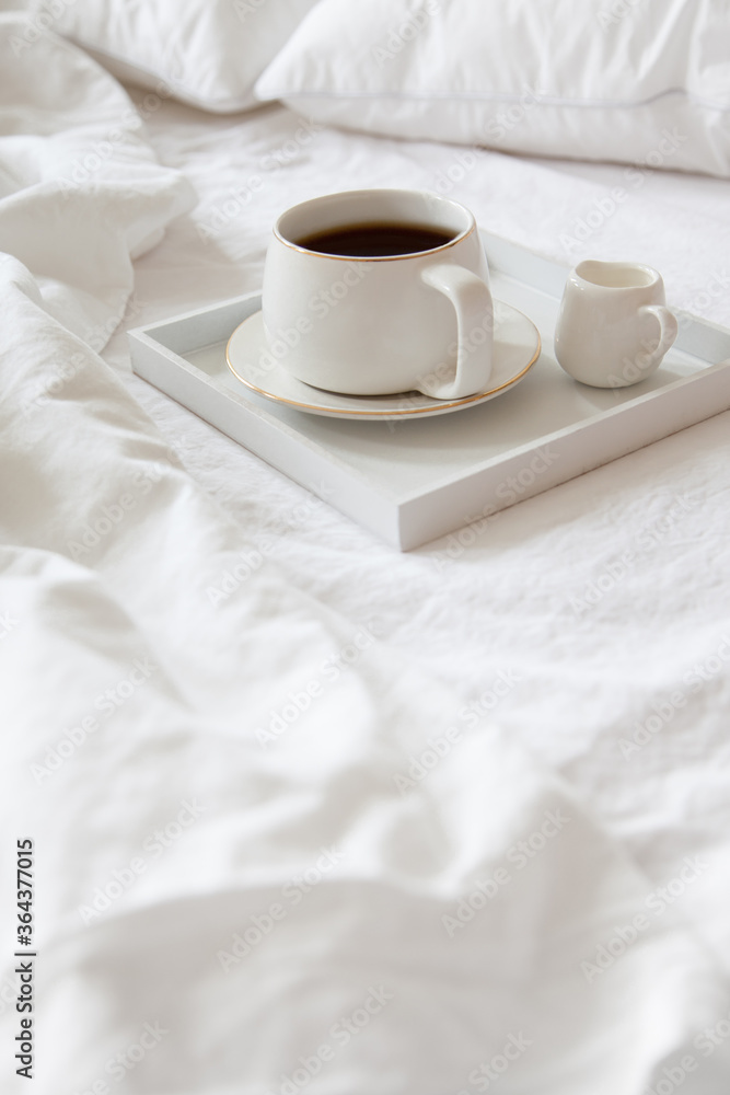 Cozy breakfast in bed, cup of coffee and milk on the grey fabric, space for text. Alarm clock for seven in the morning.
