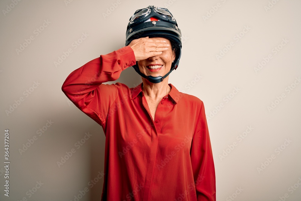 Obraz premium Middle age motorcyclist woman wearing motorcycle helmet over isolated white background smiling and laughing with hand on face covering eyes for surprise. Blind concept.