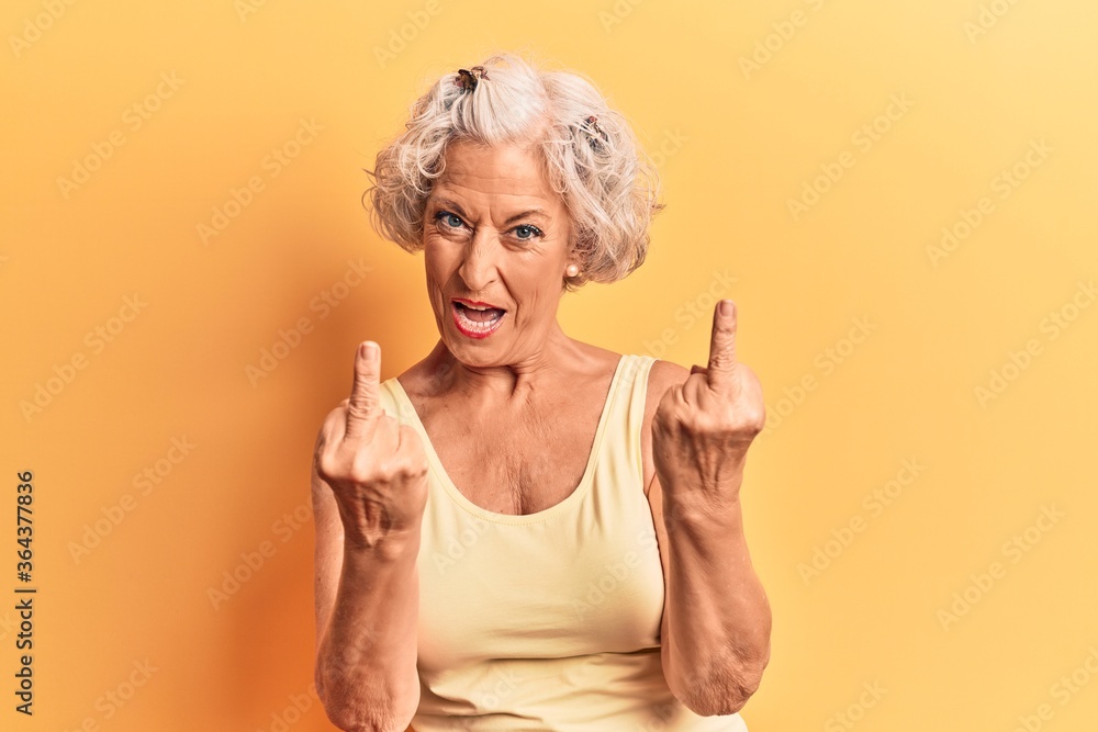Senior grey-haired woman wearing casual clothes showing middle finger doing fuck you bad expression, provocation and rude attitude. screaming excited Senior grey-haired woman wearing casual clothes showing middle finger doing fuck you bad expression, provocation and rude attitude. screaming excited
