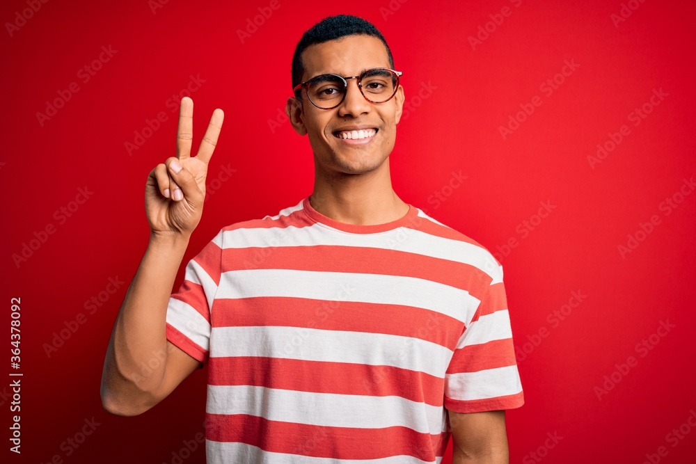 Young handsome african american man wearing casual striped t-shirt and glasses showing and pointing up with fingers number two while smiling confident and happy. Young handsome african american man wearing casual striped t-shirt and glasses showing and pointing up with fingers number two while smiling confident and happy.