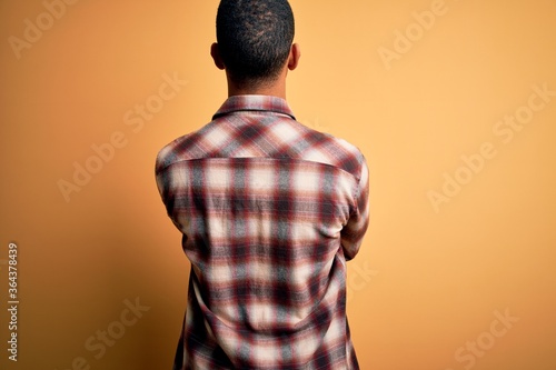 Young handsome african american man wearing casual shirt standing over yellow background standing backwards looking away with crossed arms