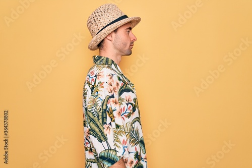 Young handsome man with blue eyes on vacation wearing summer florar shirt and hat looking to side, relax profile pose with natural face with confident smile.