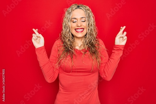Wallpaper Mural Young beautiful blonde woman wearing red casual t-shirt standing over isolated background gesturing finger crossed smiling with hope and eyes closed. Luck and superstitious concept. Torontodigital.ca
