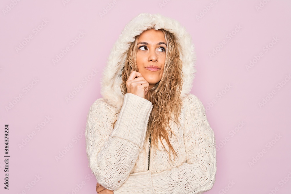 Young beautiful blonde woman wearing casual sweater with hood over isolated pink background with hand on chin thinking about question, pensive expression. Smiling with thoughtful face. Doubt concept. Young beautiful blonde woman wearing casual sweater with hood over isolated pink background with hand on chin thinking about question, pensive expression. Smiling with thoughtful face. Doubt concept.
