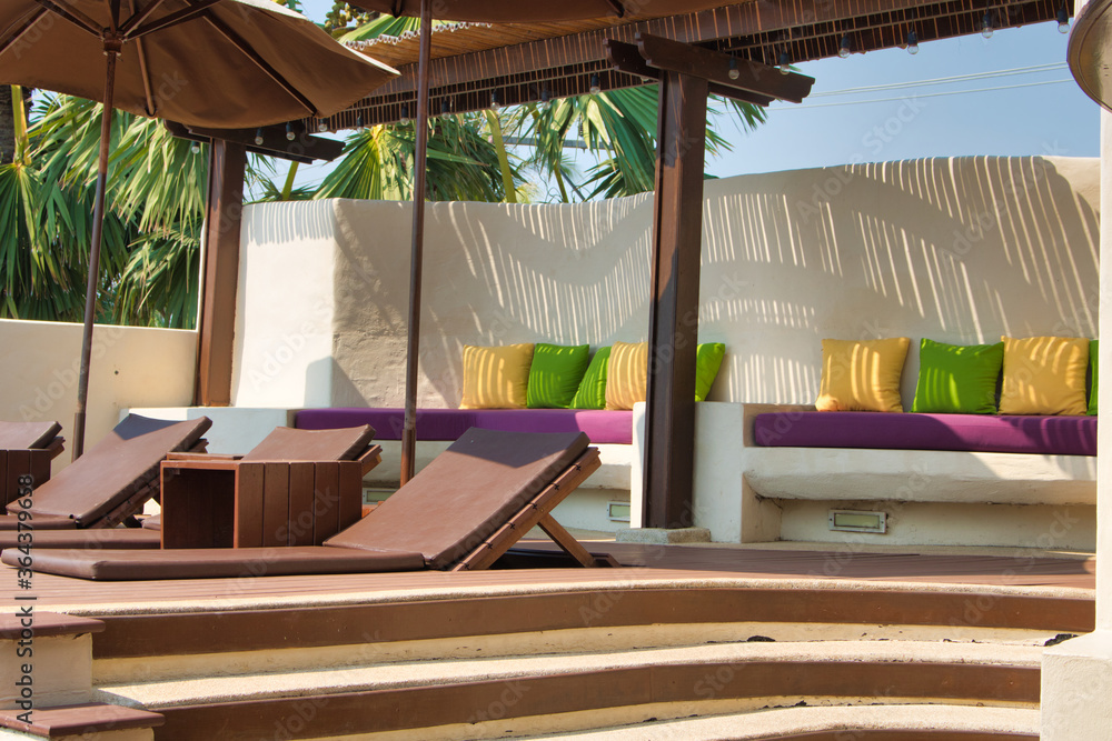 This unique photo shows a pool area with sun beds and umbrellas and a seat with decorative colorful cushions. The picture was taken in Thailand This unique photo shows a pool area with sun beds and umbrellas and a seat with decorative colorful cushions. The picture was taken in Thailand