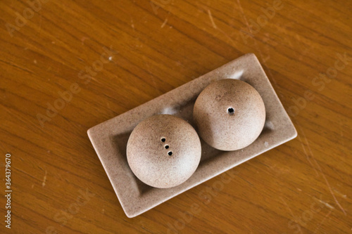 This unique photo shows a salt and pepper shaker made of stone from above in a bowl on a brown wooden table. The picture was taken in Thailand photo