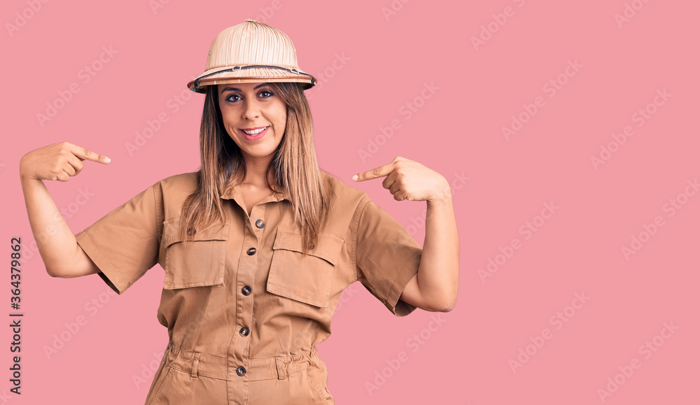 Young beautiful woman wearing explorer hat looking confident with smile on face, pointing oneself with fingers proud and happy. Young beautiful woman wearing explorer hat looking confident with smile on face, pointing oneself with fingers proud and happy.