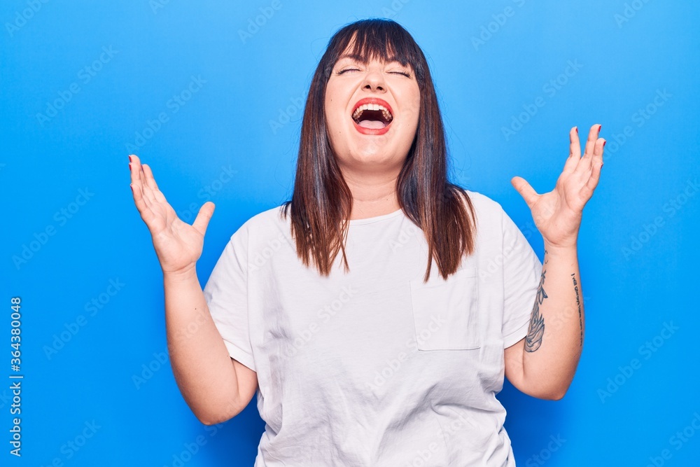 Young plus size woman wearing casual clothes celebrating mad and crazy for success with arms raised and closed eyes screaming excited. winner concept Young plus size woman wearing casual clothes celebrating mad and crazy for success with arms raised and closed eyes screaming excited. winner concept