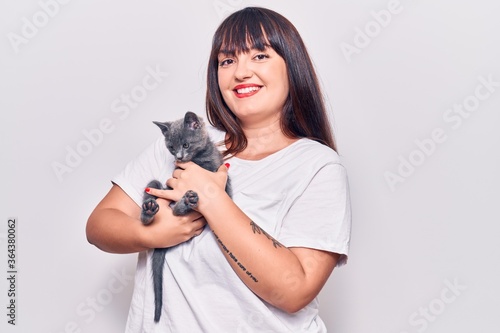 Young beautiful plus size woman smilling happy and confident. Standing with smile on face holding adorable cat over isolated white background photo