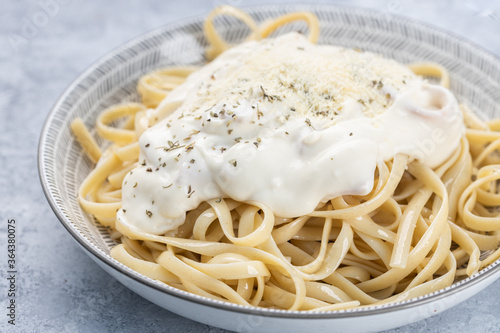 Close up of plate of pasta a la carbonara with parmesan cheese, served on a rustic textured plate, on a rustic wooden background.