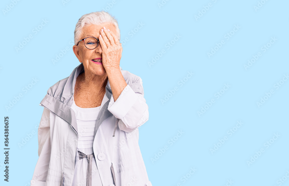 Senior beautiful woman with blue eyes and grey hair wearing casual clothes and glasses covering one eye with hand, confident smile on face and surprise emotion. Senior beautiful woman with blue eyes and grey hair wearing casual clothes and glasses covering one eye with hand, confident smile on face and surprise emotion.