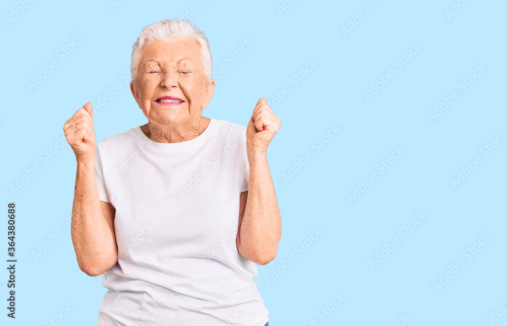 Senior beautiful woman with blue eyes and grey hair wearing casual white tshirt excited for success with arms raised and eyes closed celebrating victory smiling. winner concept. Senior beautiful woman with blue eyes and grey hair wearing casual white tshirt excited for success with arms raised and eyes closed celebrating victory smiling. winner concept.