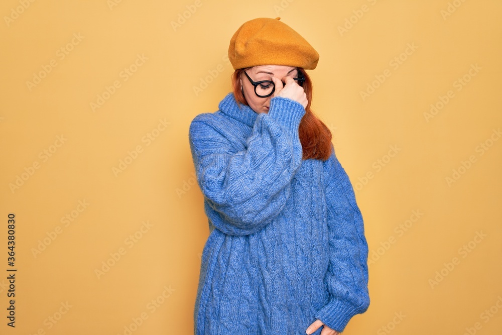 Obraz premium Young beautiful redhead woman wearing french beret and glasses over yellow background tired rubbing nose and eyes feeling fatigue and headache. Stress and frustration concept.