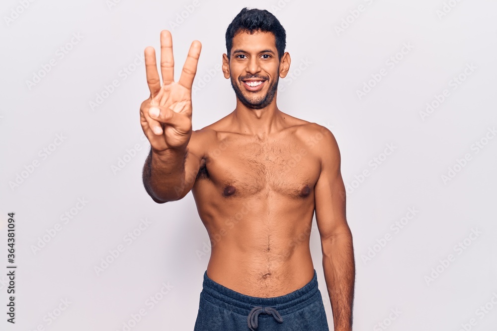 Young latin man standing shirtless showing and pointing up with fingers number three while smiling confident and happy.