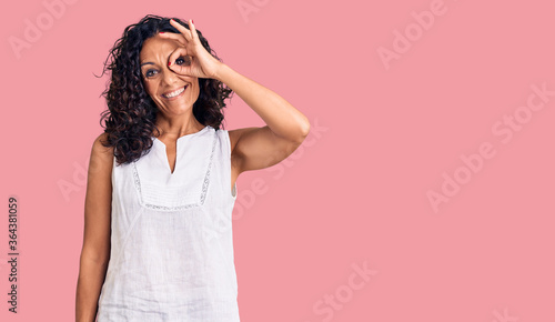 Middle age beautiful woman wearing casual sleeveless t shirt smiling happy doing ok sign with hand on eye looking through fingers