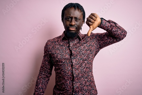 Young handsome african american man wearing casual shirt standing over pink background looking unhappy and angry showing rejection and negative with thumbs down gesture. Bad expression.