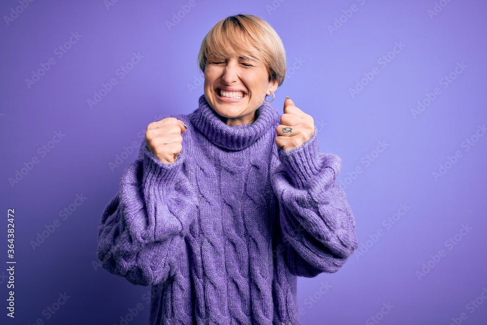 Young blonde woman with short hair wearing winter turtleneck sweater over purple background excited for success with arms raised and eyes closed celebrating victory smiling. Winner concept. Young blonde woman with short hair wearing winter turtleneck sweater over purple background excited for success with arms raised and eyes closed celebrating victory smiling. Winner concept.
