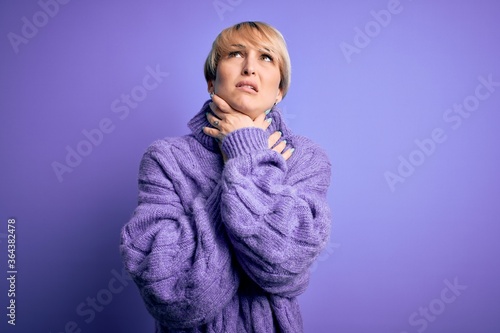 Young blonde woman with short hair wearing winter turtleneck sweater over purple background shouting suffocate because painful strangle. Health problem. Asphyxiate and suicide concept.