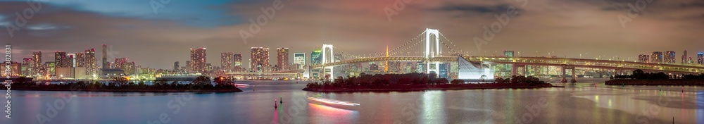 Tokyo Destinations. View of Renowned Rainbow Bridge in Odaiba Island in Tokyo At Twilight with Line of Skyscrapers in Background.
