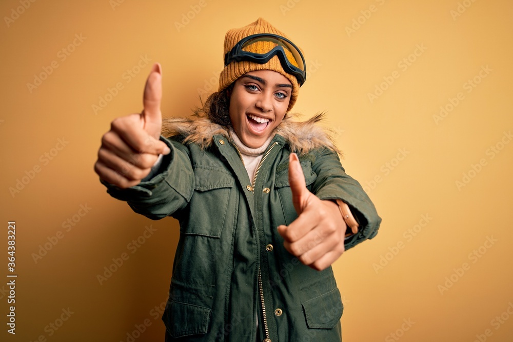Young african american afro skier girl wearing snow sportswear and ski goggles approving doing positive gesture with hand, thumbs up smiling and happy for success. Winner gesture. Young african american afro skier girl wearing snow sportswear and ski goggles approving doing positive gesture with hand, thumbs up smiling and happy for success. Winner gesture.