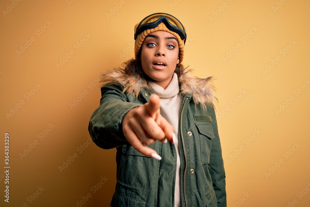 Young african american afro skier girl wearing snow sportswear and ski goggles pointing displeased and frustrated to the camera, angry and furious with you