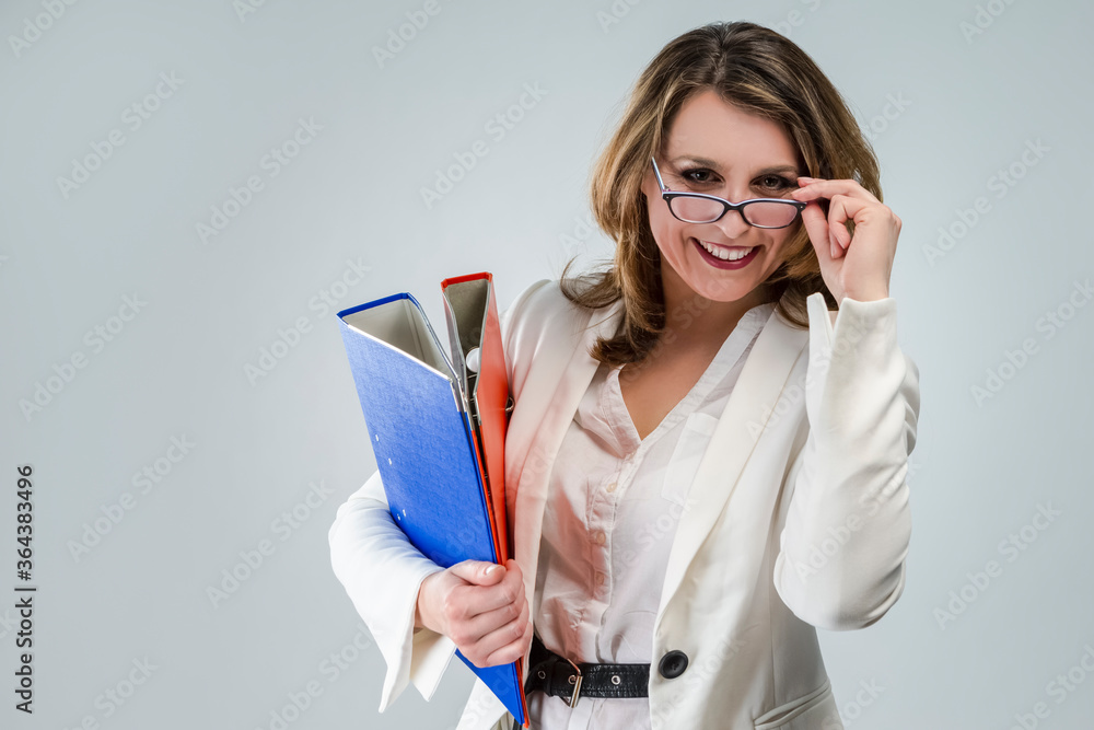 Females In Business Concepts. Portrait of Cute and Smiling Mature Caucasian Business Woman in White Jacket With Colorful Folders Against White Background. Females In Business Concepts. Portrait of Cute and Smiling Mature Caucasian Business Woman in White Jacket With Colorful Folders Against White Background.