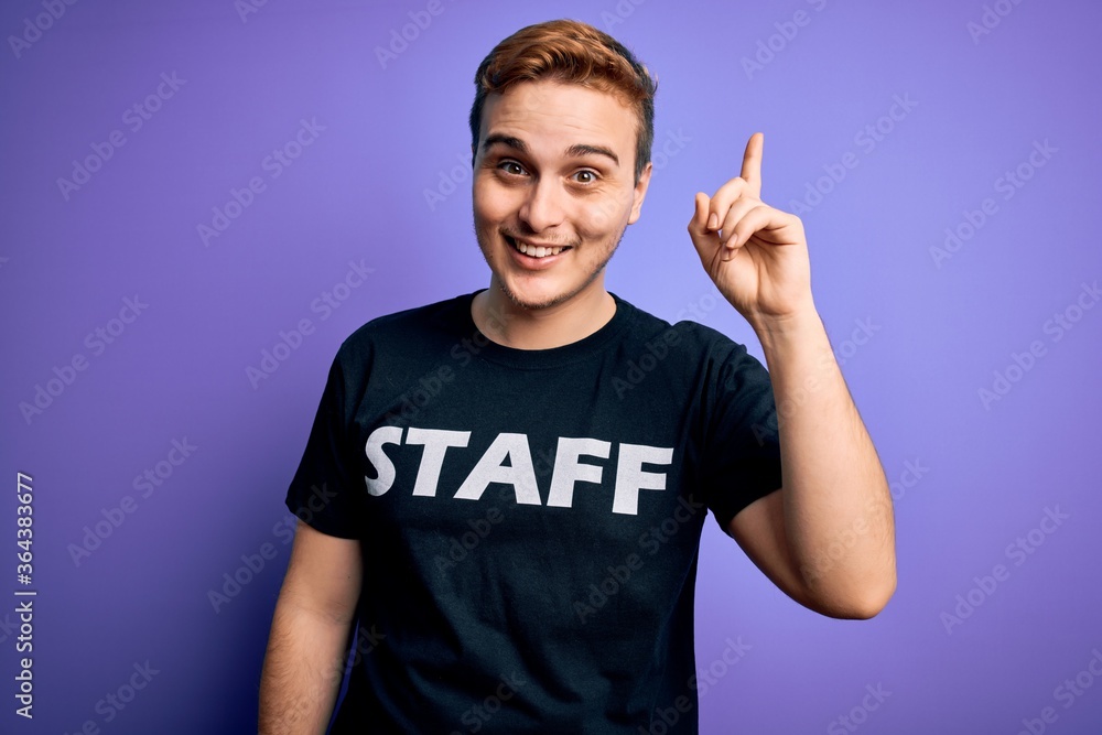Young handsome redhead worker man wearing staff t-shirt uniform over purple background pointing finger up with successful idea. Exited and happy. Number one. Young handsome redhead worker man wearing staff t-shirt uniform over purple background pointing finger up with successful idea. Exited and happy. Number one.
