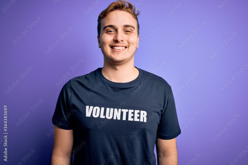 Obraz premium Young handsome redhead man wearing volunteer t-shirt over isolated purple background looking positive and happy standing and smiling with a confident smile showing teeth