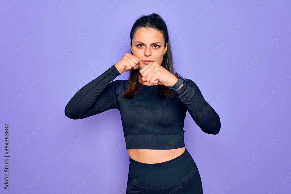 Young beautiful brunette sporty woman wearing casual sportswear over purple background Punching fist to fight, aggressive and angry attack, threat and violence Young beautiful brunette sporty woman wearing casual sportswear over purple background Punching fist to fight, aggressive and angry attack, threat and violence