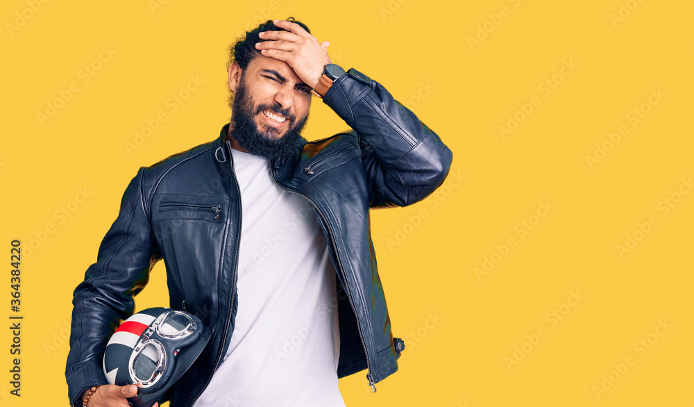 Naklejka premium Young arab man holding motorcycle helmet stressed and frustrated with hand on head, surprised and angry face