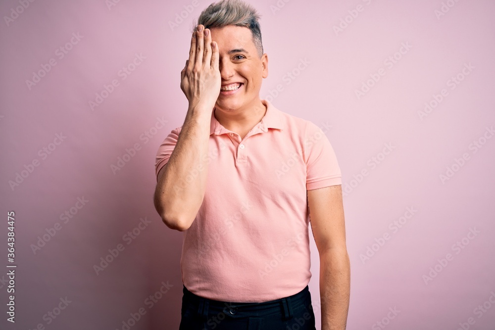 Young handsome modern man wearing casual pink t-shirt over isolated background covering one eye with hand, confident smile on face and surprise emotion. Young handsome modern man wearing casual pink t-shirt over isolated background covering one eye with hand, confident smile on face and surprise emotion.