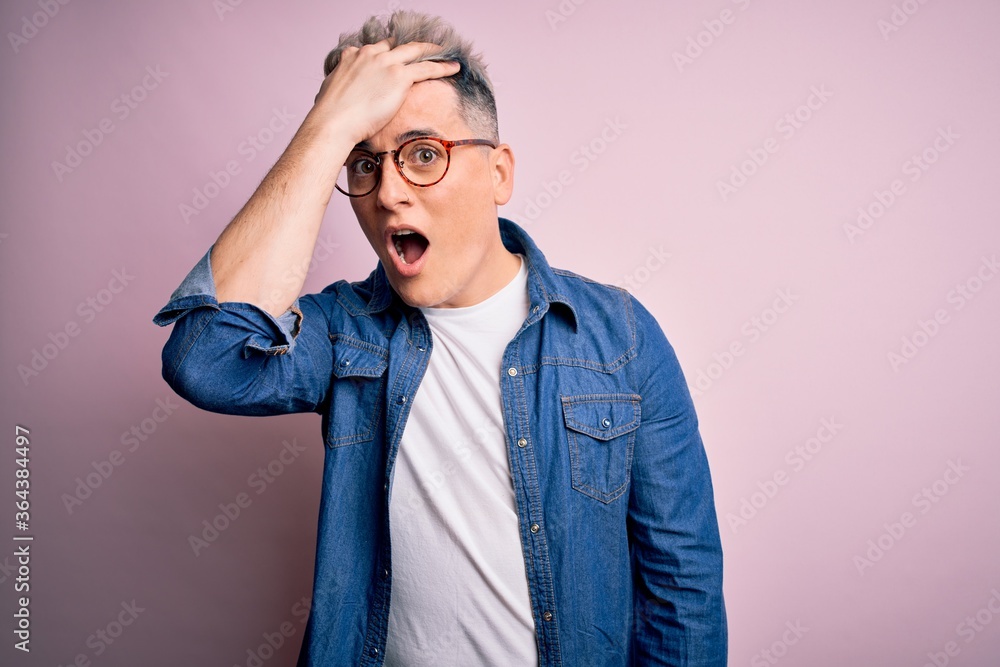 Young handsome modern man wearing glasses and denim jacket over pink isolated background surprised with hand on head for mistake, remember error. Forgot, bad memory concept. Young handsome modern man wearing glasses and denim jacket over pink isolated background surprised with hand on head for mistake, remember error. Forgot, bad memory concept.