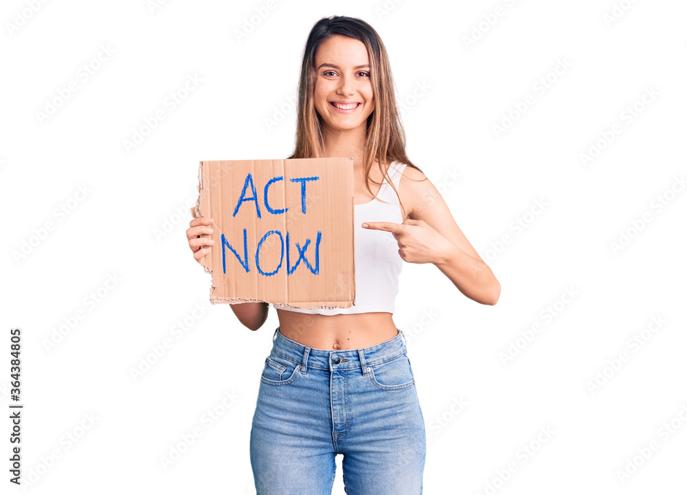 Young beautiful girl holding act now banner smiling happy pointing with hand and finger Young beautiful girl holding act now banner smiling happy pointing with hand and finger