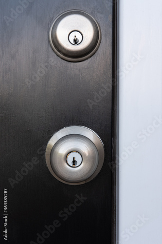Fotografie Photograph of a locking door knob and deadbolt on a black painted door with a wh