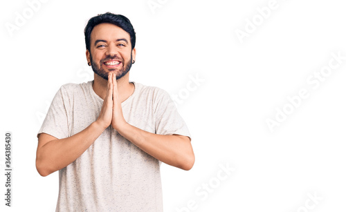 Young hispanic man wearing casual clothes praying with hands together asking for forgiveness smiling confident.