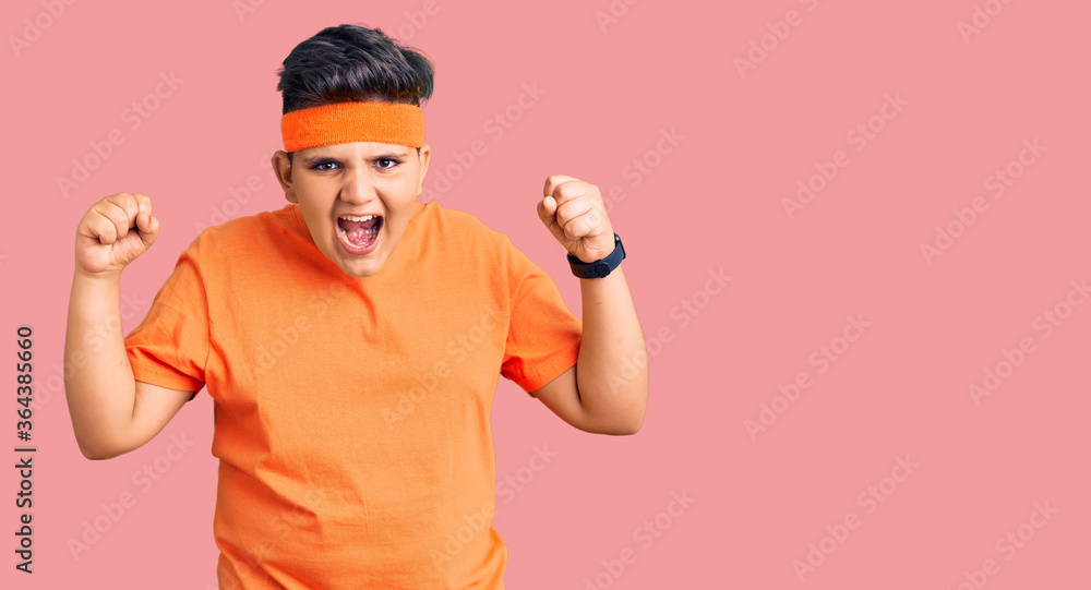 Little boy kid wearing sportswear angry and mad raising fists frustrated and furious while shouting with anger. rage and aggressive concept.
