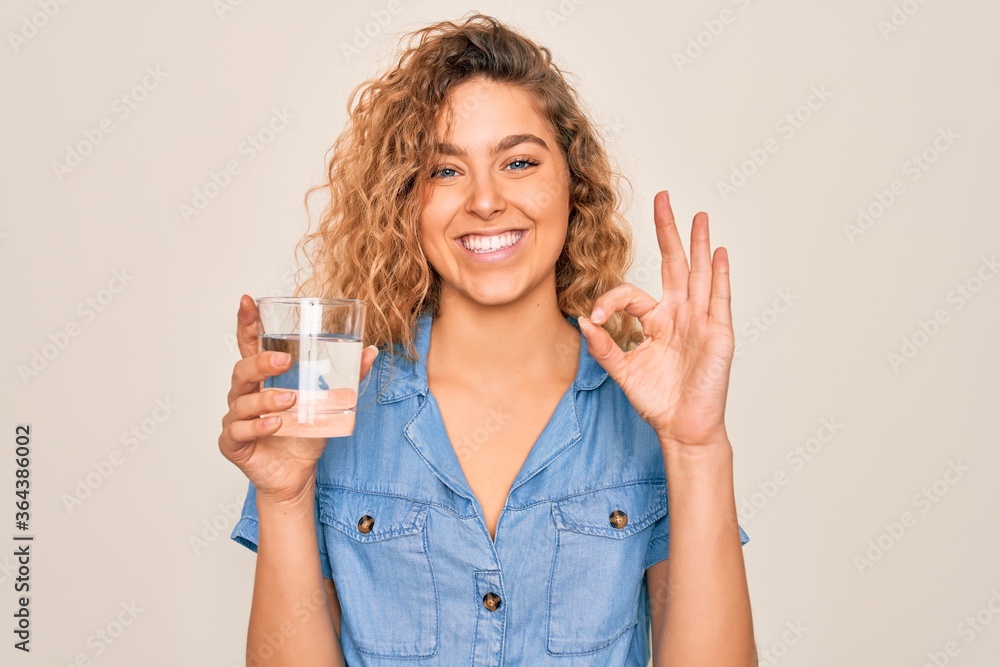 Young beautiful blonde woman with blue eyes drinking glass of water over white background doing ok sign with fingers, excellent symbol Young beautiful blonde woman with blue eyes drinking glass of water over white background doing ok sign with fingers, excellent symbol