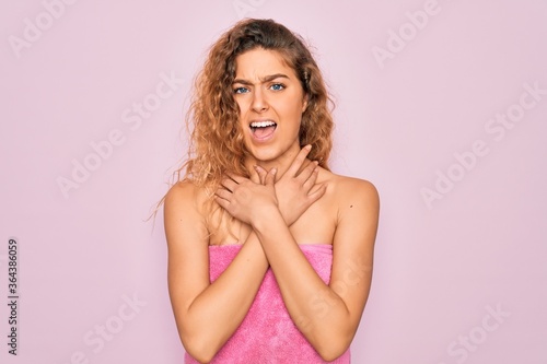 Beautiful blonde woman with blue eyes wearing towel shower after bath over pink background shouting and suffocate because painful strangle. Health problem. Asphyxiate and suicide concept.