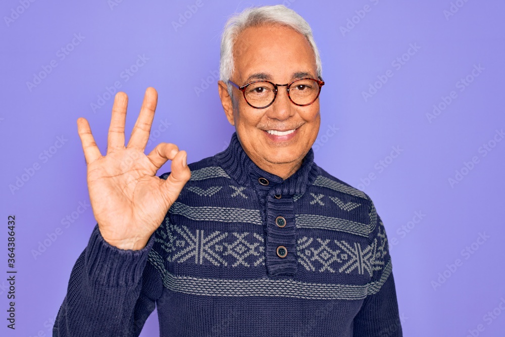Naklejka premium Middle age senior grey-haired man wearing glasses and winter sweater over purple background smiling positive doing ok sign with hand and fingers. Successful expression.