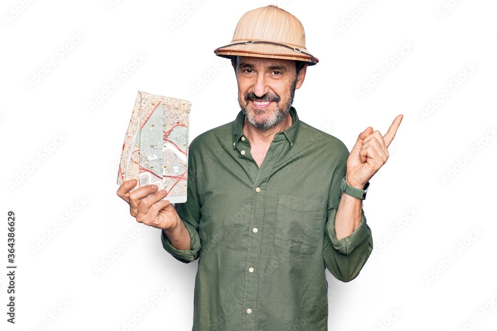 Middle age handsome tourist man on vacation wearing explorer hat holding city map smiling happy pointing with hand and finger to the side Middle age handsome tourist man on vacation wearing explorer hat holding city map smiling happy pointing with hand and finger to the side